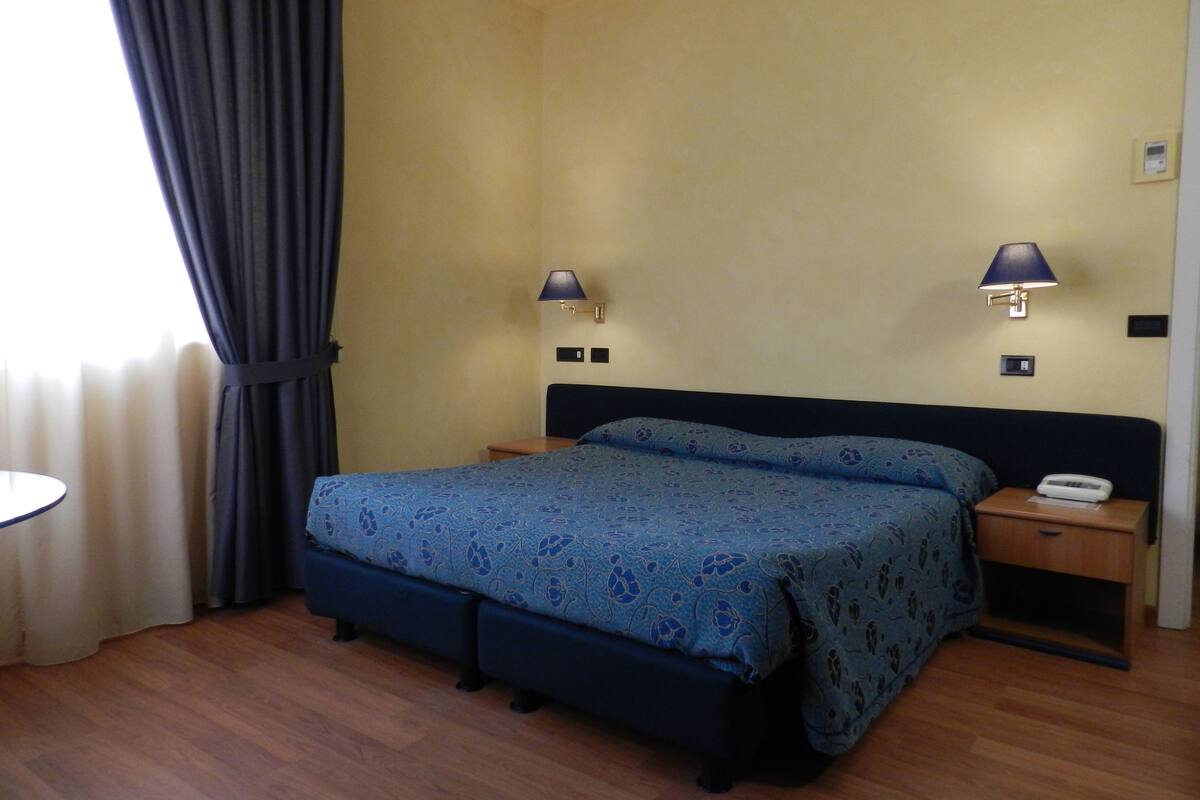 Ein Hotelzimmer mit Bett, Nachttischen, Lampen und einem Fenster mit Vorhängen.