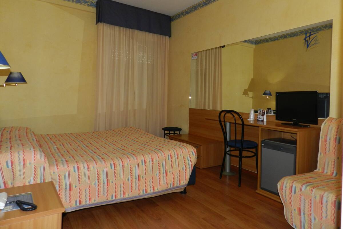Ein Hotelzimmer mit Bett, Schreibtisch, Stuhl, Fernseher und kleinem Kühlschrank.