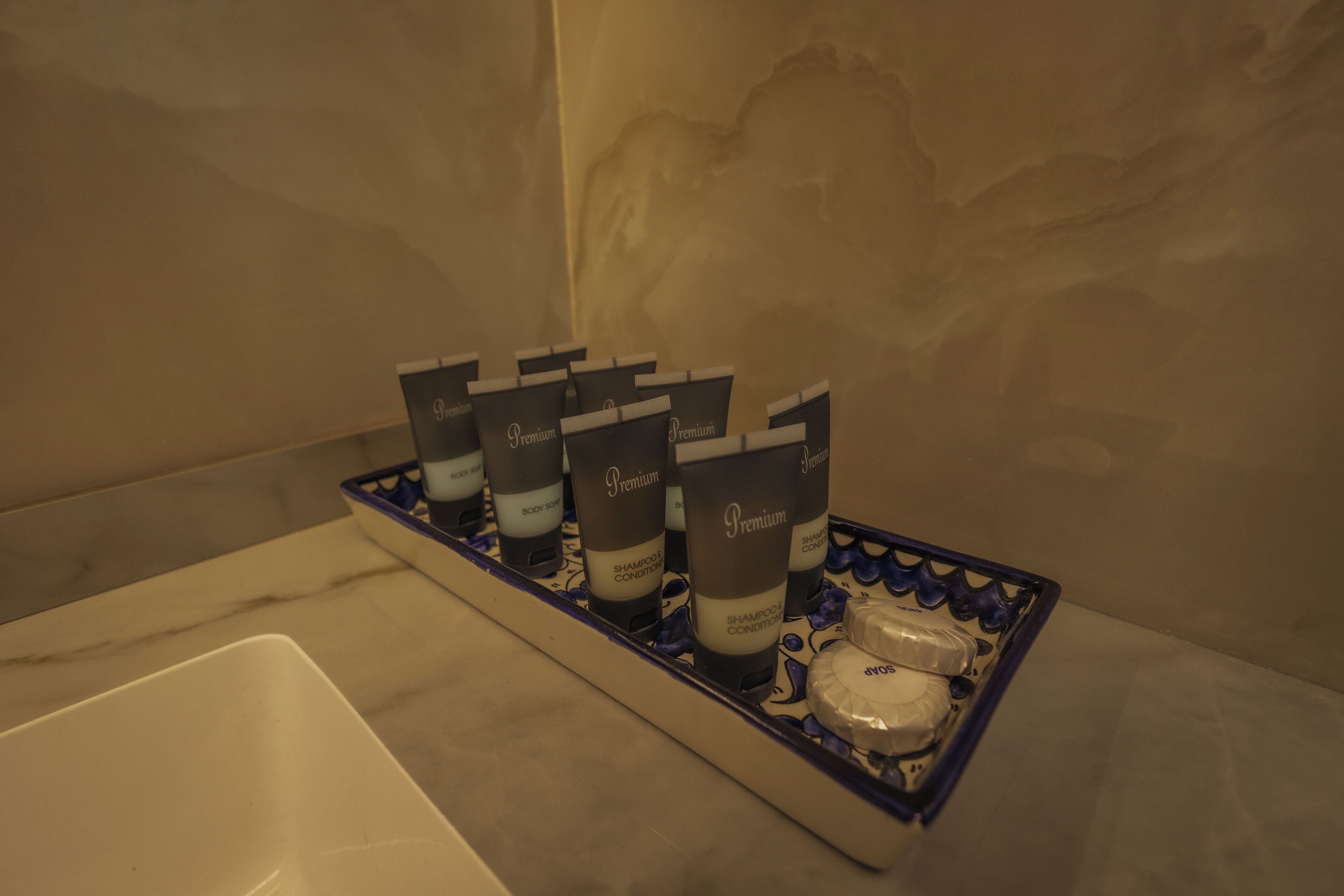 A bathroom with a marble sink and a tray holding several bottles of shampoo conditioner.
