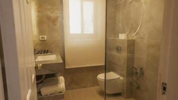 Un baño moderno con cabina de ducha de vidrio, un inodoro y un lavamanos con toallero.