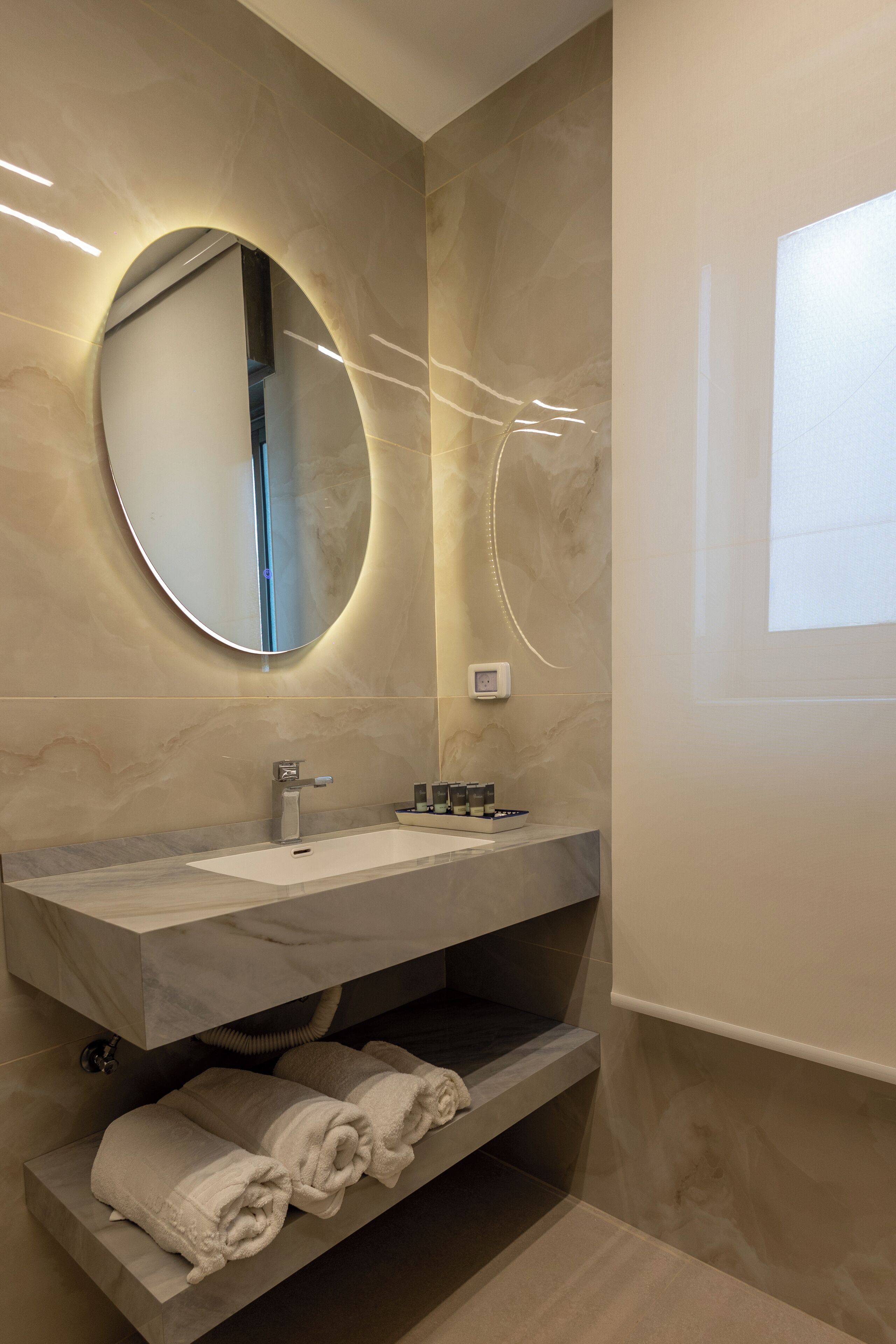 Une salle de bain moderne avec un meuble-lavabo en marbre, un miroir rond et un porte-serviettes.