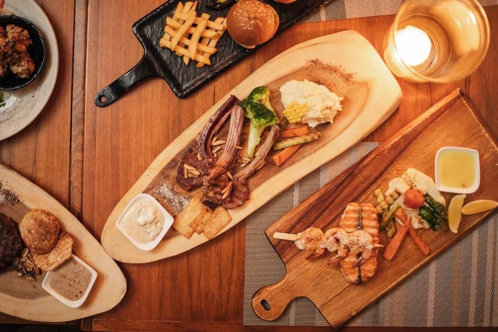 A wooden table with various dishes including grilled meat, vegetables, and sauces.