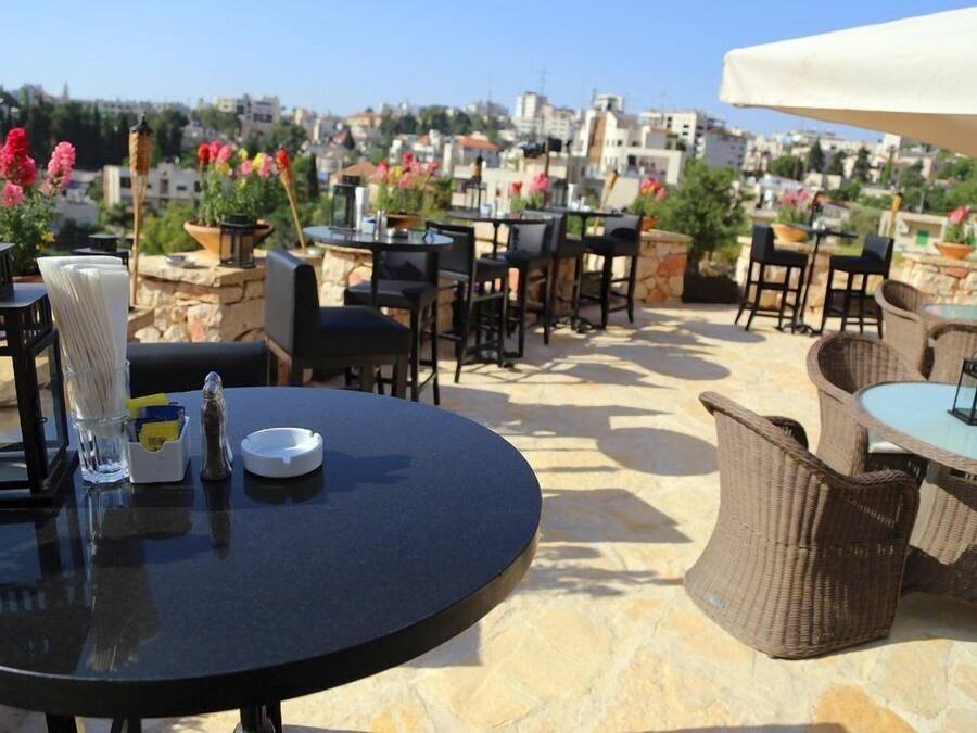 Eine Terrasse im Freien mit runden Tischen und Korbstühlen vor einer Stadtkulisse.