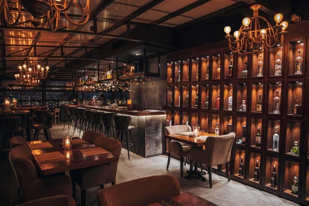 A bar area with wooden shelves displaying bottles, a bar counter, and seating arrangements.