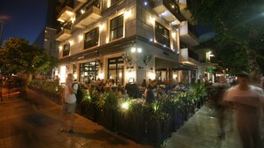 Un immeuble à plusieurs étages abritant un restaurant au rez-de-chaussée, avec une terrasse et des plantes en pot.