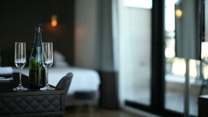 Une chambre d’hôtel avec un lit, une table sur laquelle se trouvent une bouteille et des verres, et une vue dégagée grâce à de grandes fenêtres.