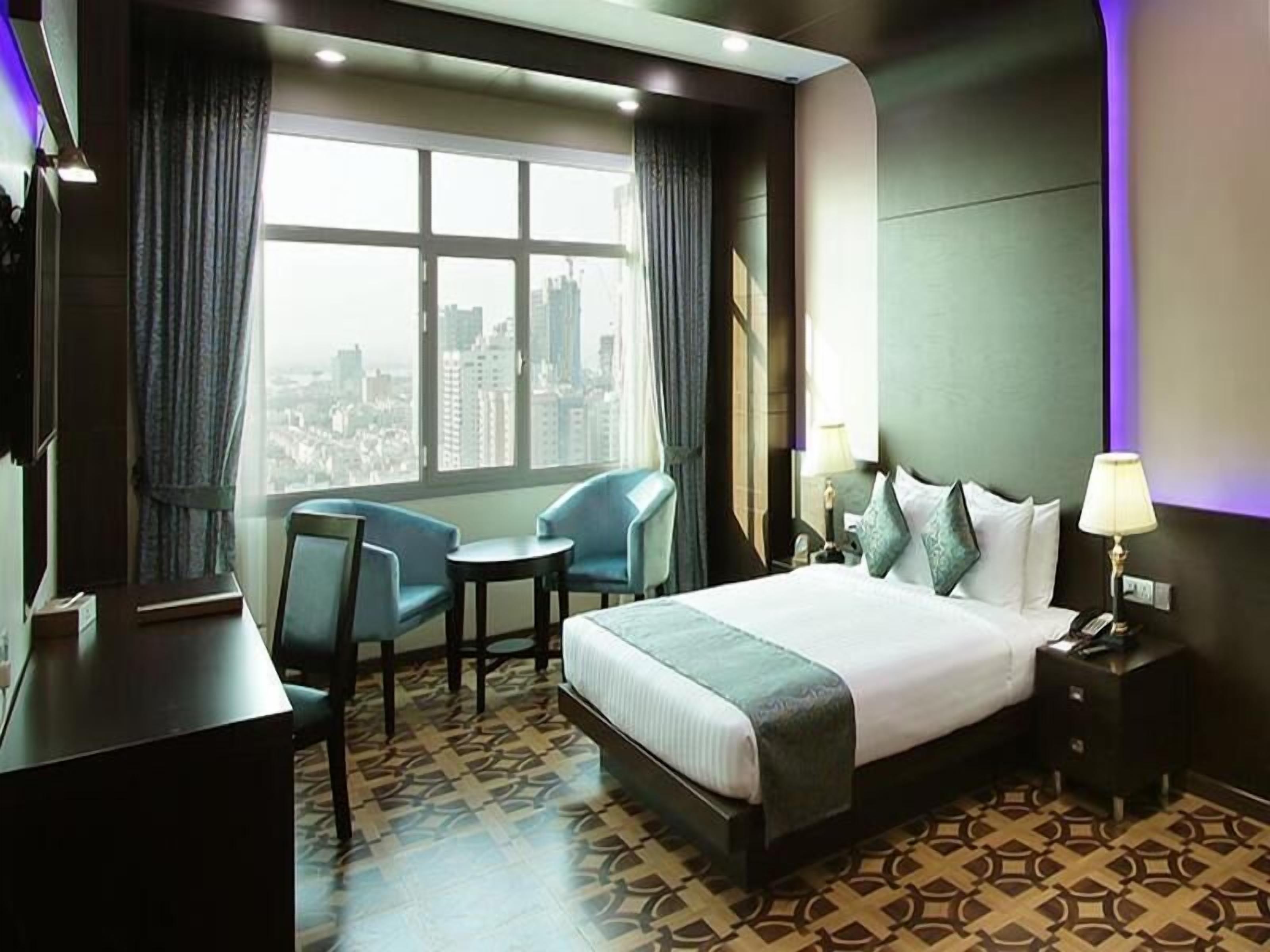 A hotel room with a large bed, two armchairs, a desk, and a view of the city.