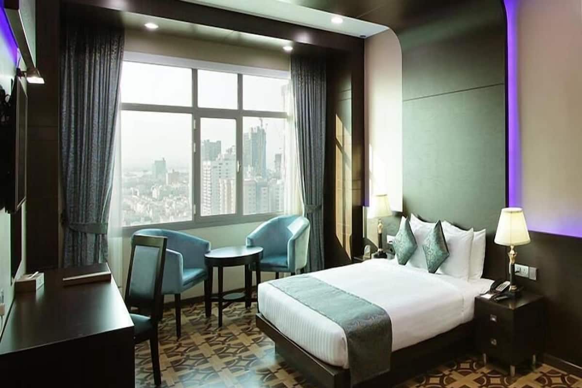 Ein Hotelzimmer mit einem großen Bett, zwei Sesseln, einem Schreibtisch und Blick auf die Stadt.