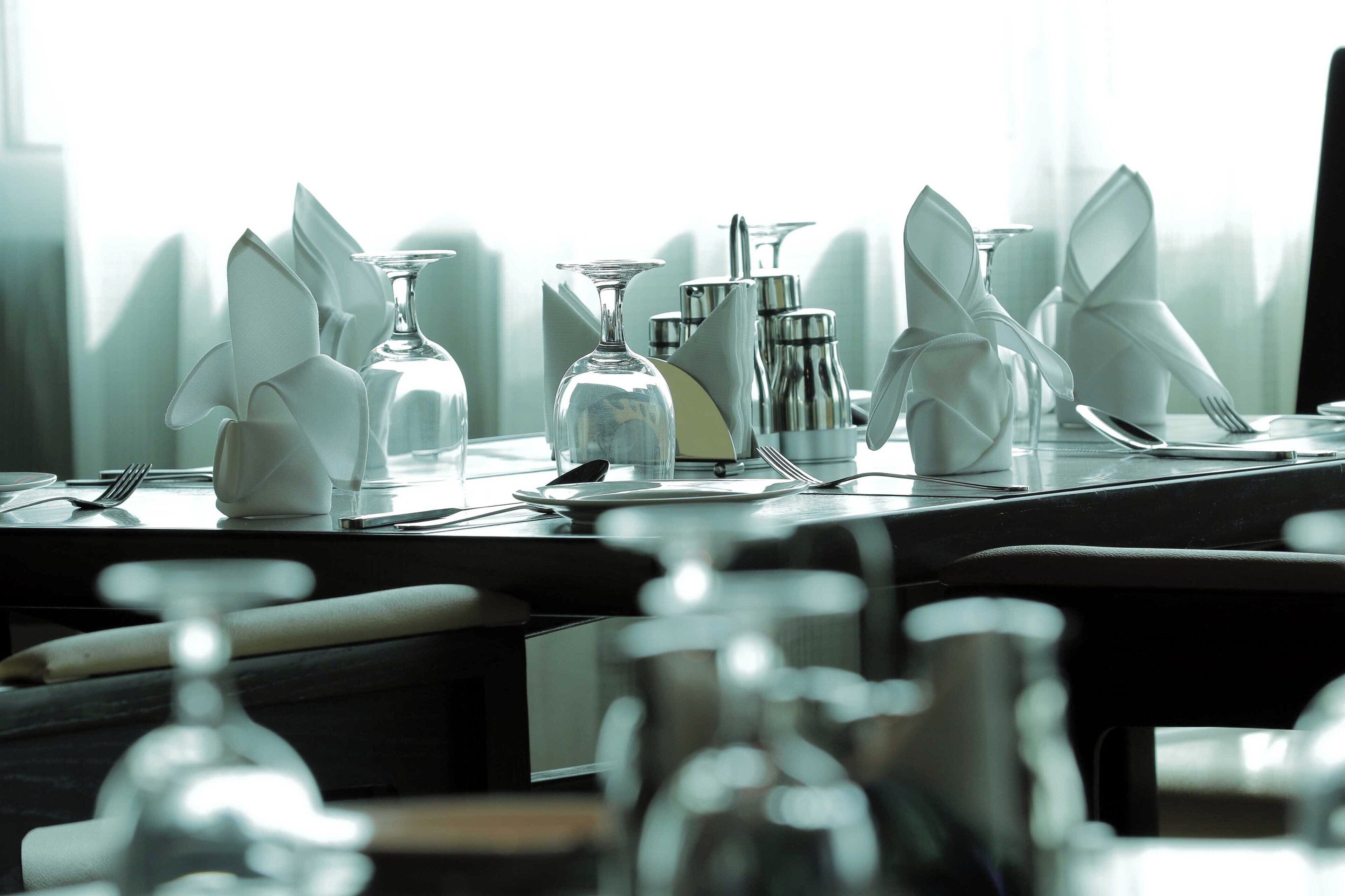 Una mesa preparada para una comida, con vasos transparentes, cubiertos y servilletas dobladas.