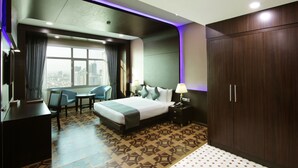 A hotel room with a large bed, a desk, a chair, a nightstand with a lamp, and a wardrobe. - Park Regis Lotus Hotel (Manama)