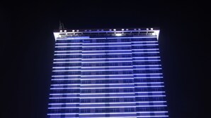 A tall hotel with a modern design, featuring horizontal blue LED lighting and a prominent sign for the Park Regis Lotus Hotel. - Park Regis Lotus Hotel (Manama)