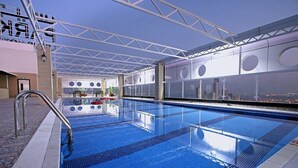 An indoor swimming pool with clear blue water, a metal handrail, and a city view through large windows. - Park Regis Lotus Hotel (Manama)