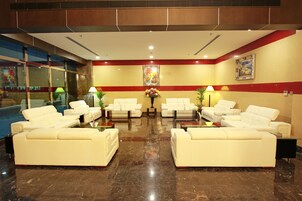 Un hall con sofás de cuero blanco dispuestos en forma de U, suelo de mármol pulido y una mesa central con un jarrón de flores.
