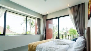 A hotel room with a bed, large windows, and a view of palm trees. - Nitchanan Villa (Ko Pha-ngan)