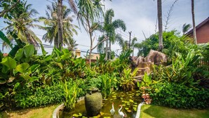A garden with a pond, lush greenery, and a large decorative vase. - Nitchanan Villa (Ko Pha-ngan)