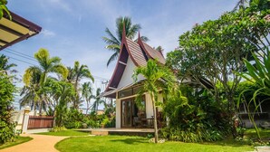 A house with a sloped roof, surrounded by lush greenery and palm trees. - Nitchanan Villa (Ko Pha-ngan)