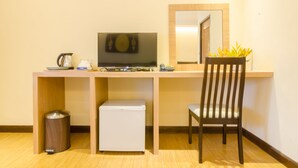 Habitació d'hotel senzilla amb escriptori de fusta, televisió, nevera petita, cadira i paperera.