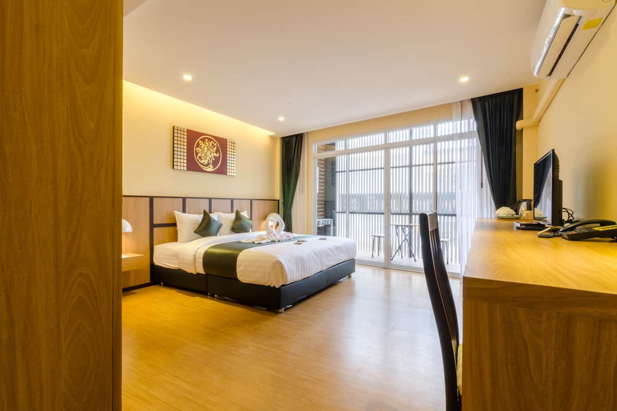 Una habitación de hotel con cama, escritorio, silla, televisor y ventana con cortinas.