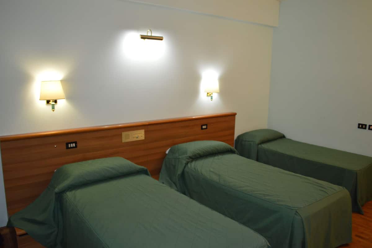 A hotel room with two single beds, wooden headboard, and two wall-mounted night lights.