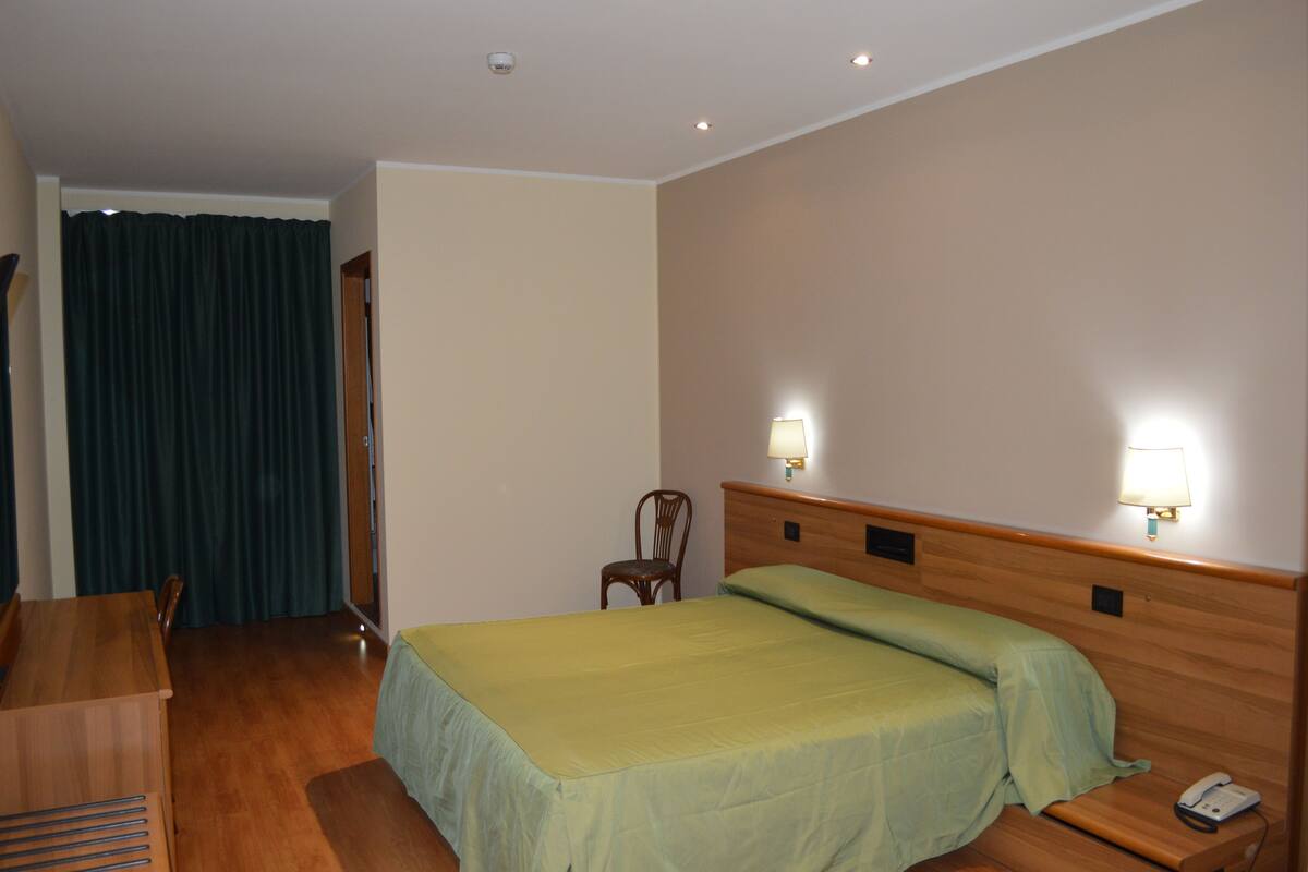 A hotel room with a bed, a chair, a desk, and a telephone.