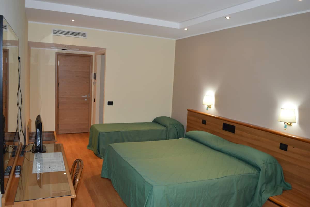 A hotel room with two single beds, a wooden headboard, a desk with a computer and remote controls, and a mirror.
