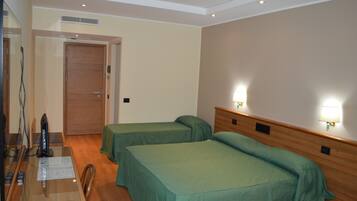 A hotel room with two single beds, a wooden headboard, a desk with a computer and remote controls, and a mirror.