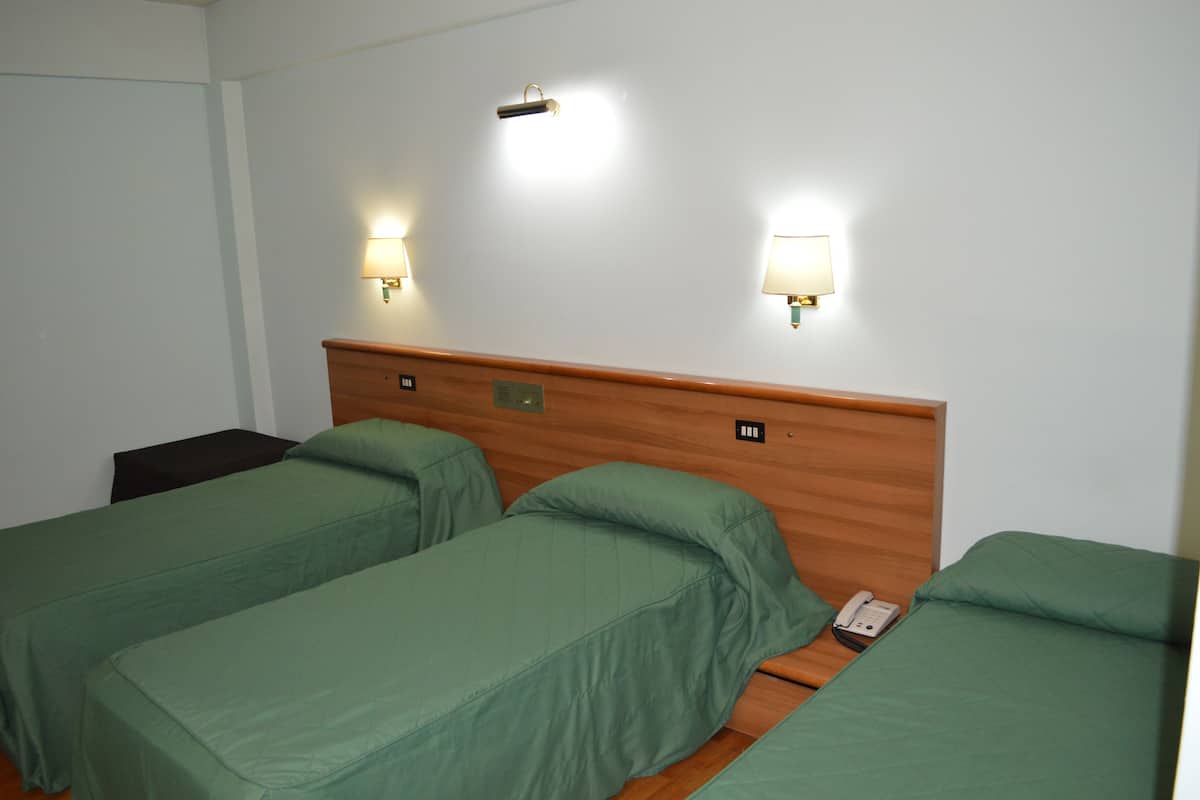 A hotel room with two single beds, each with a green bedspread and pillows, a wooden headboard, and two wall-mounted night lights.