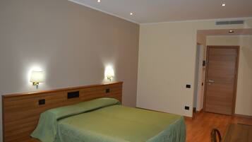 A hotel room with a single bed, two bedside lamps, a wooden headboard, a wooden table, and a door.