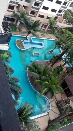 Una piscina con diseño singular, rodeada de palmeras y un edificio de varios pisos al fondo.