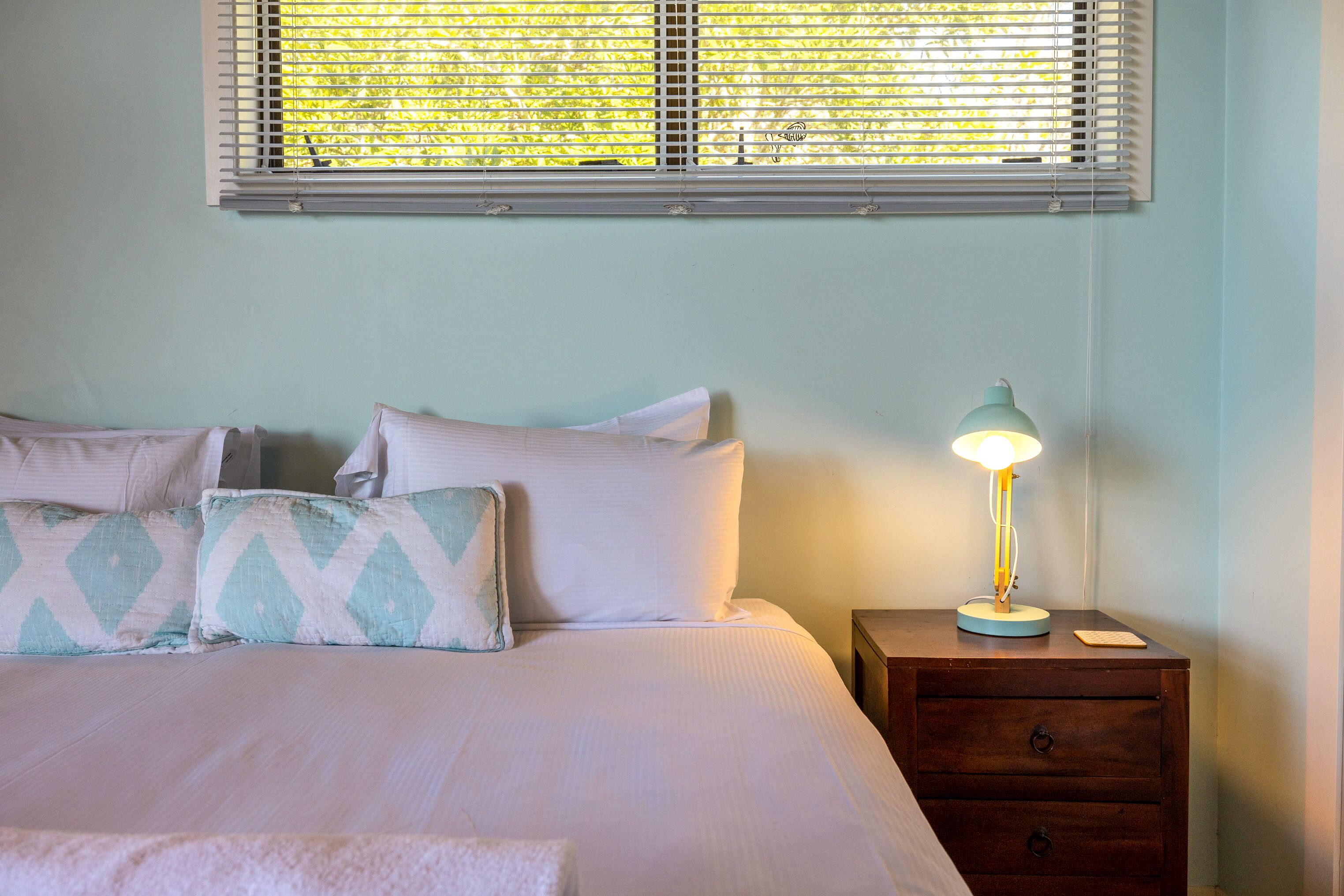 A neatly made bed with pillows, a bedside lamp, and a nightstand with drawers.