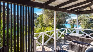 Uma área externa coberta com móveis de vime e vista para uma piscina e vegetação.