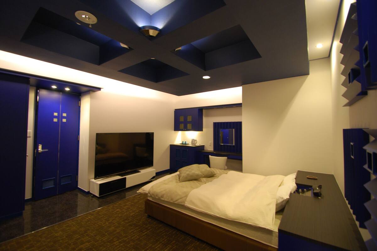 A modern hotel room with a large bed, a flat-screen TV, a desk, and a wardrobe.