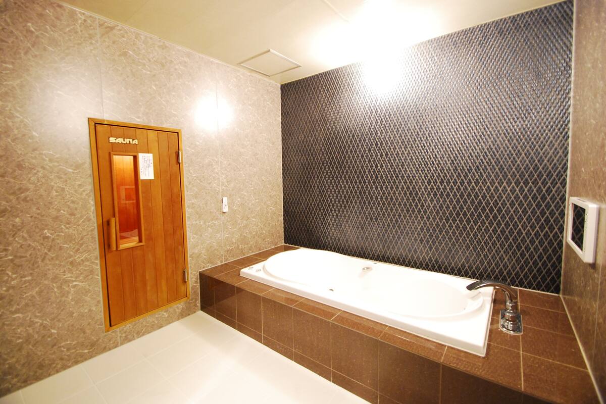 A modern bathroom with a large bathtub, a wooden door labeled "SAUNA", and a textured wall.