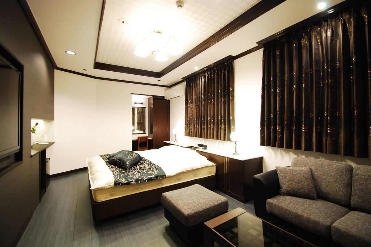 A modern hotel room with a large bed, a sofa, a desk, and a mirror.