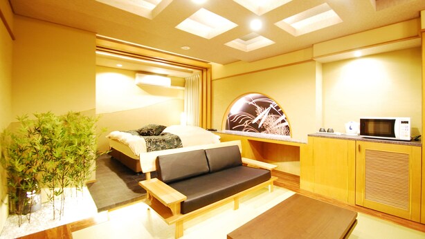 A modern hotel room with a sofa, a dining table, a microwave, and a potted plant. - Hotel Free Style Okayama (Okayama)