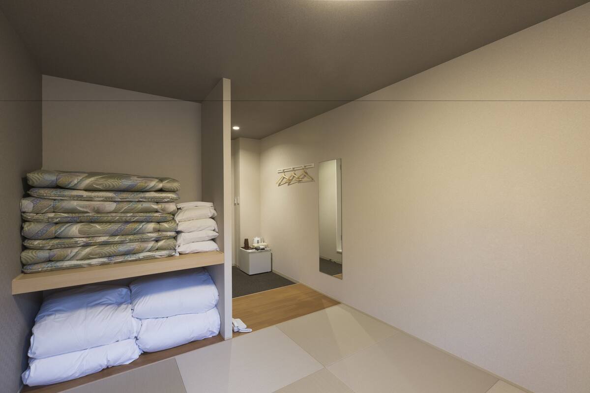 A hotel room with a neatly folded bed, a bedside table with a lamp, and a mirror on the wall.