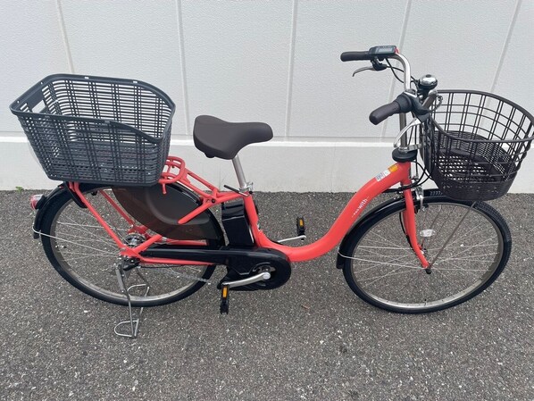 Una bicicleta roja con dos canastos, uno delantero y otro trasero, estacionada junto a una pared.