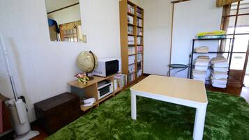 A room with a green carpet, a white table, a bookshelf, a mirror, and a window with blinds.
