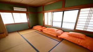 Una habitación con suelo de tatami, pantalla corredera shoji, tatamis y cojines naranjas.