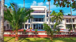 A modern two-story building with a swimming pool, surrounded by palm trees and a red-tiled pool deck. - Costa Palawan Resort (Puerto Princesa)