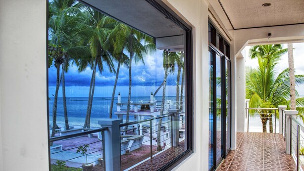 A balcony with a view of the ocean and palm trees. - Costa Palawan Resort (Puerto Princesa)