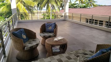 A covered balcony with wicker furniture, a tiled floor, and a view of palm trees and a beach.
