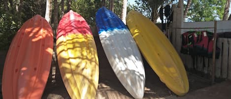 Four surfboards leaning against a wooden structure in a shaded area with trees in the background.