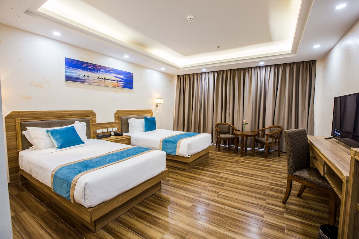 A hotel room with two beds, a desk, a chair, a television, and a painting on the wall.