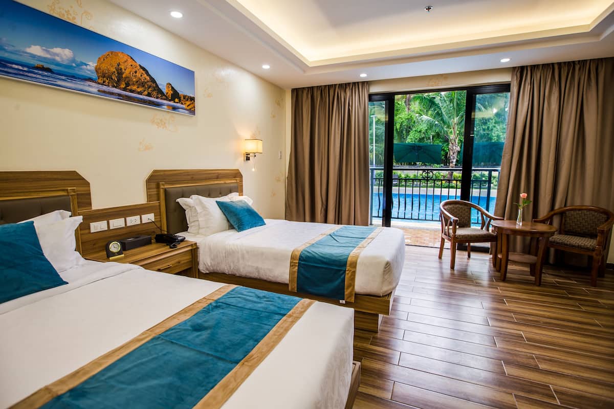 A hotel room with two beds, a wooden floor, a painting on the wall, a balcony with a view of the pool, and a table with chairs.