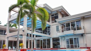 A modern multi-story hotel with a swimming pool, outdoor seating, and palm trees. - Costa Palawan Resort (Puerto Princesa)