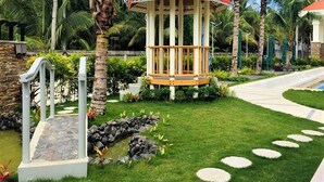 A gazebo with a red roof, surrounded by a well-maintained garden with palm trees and a stone pathway. - Costa Palawan Resort (Puerto Princesa)