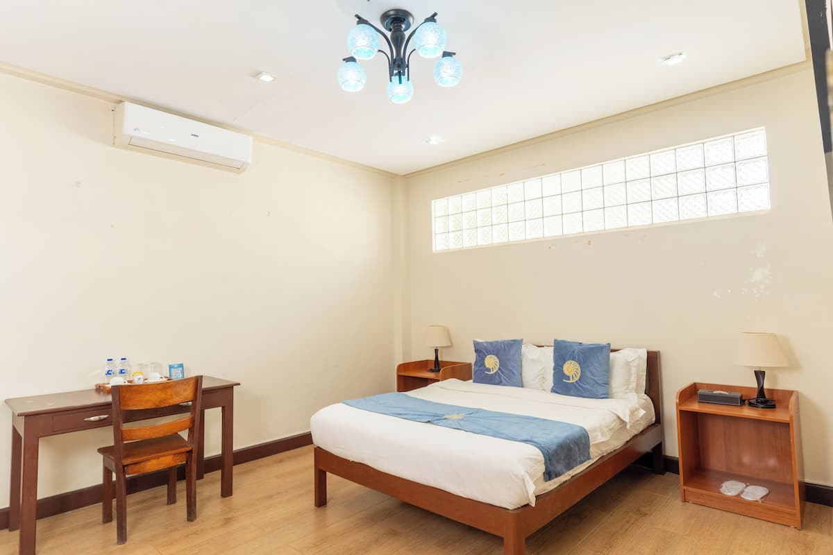 A hotel room with a bed, a desk, a chair, a window, and a ceiling light fixture.