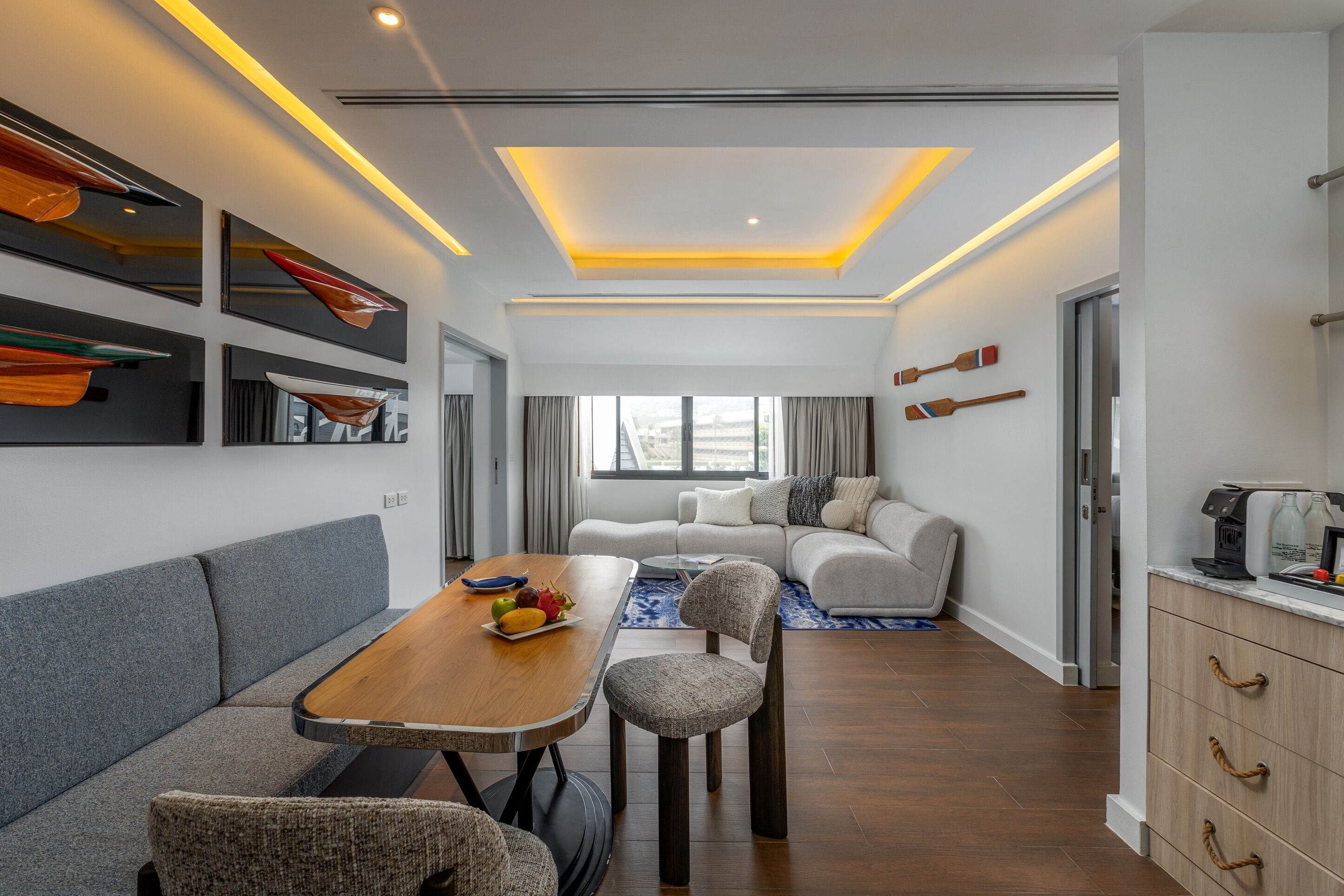 A modern living room with a dining area, a sofa, a coffee machine, and a view of the outdoors.