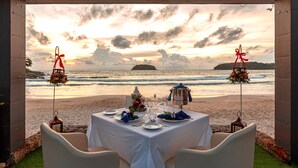 Mesa posta para dois, com vista para o oceano ao pôr do sol.